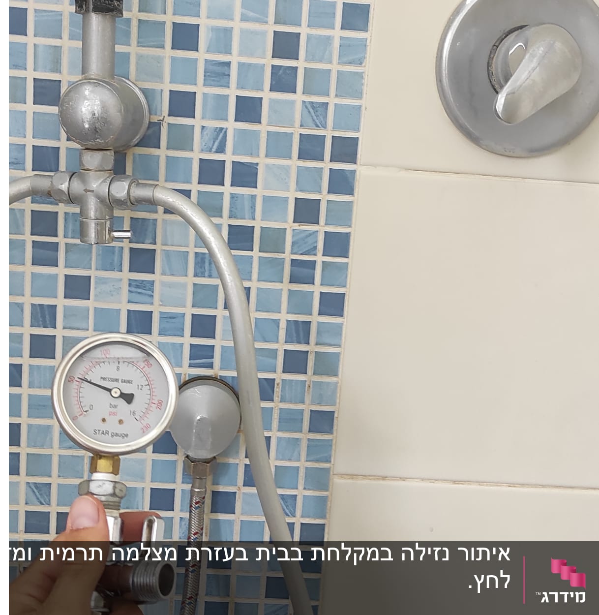 מד לחץ מים מוחזק ביד ליד צינור במקלחת